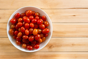 fresh cherry tomatoes in white ceramic bowl on wooden table background.