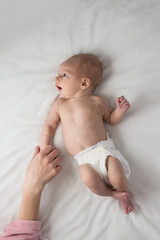 A Little Baby in a Diaper, Baby, lies on a white bed and a Woman's Hand. White background. Flat lay, top view