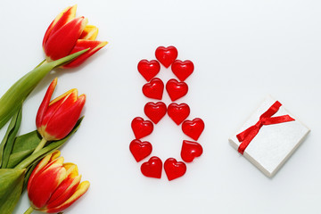 Card on March 8 - International Women's Day: Three red tulips present with a bow and number "8" lined with decorative hearts on a white background