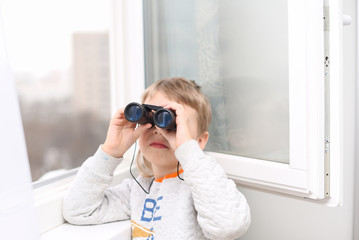 ittle boy looking through the window with binoculars