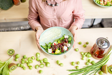 Holding a salad with beet and cheese on the wooden table with green ingredients and tea pot