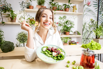 Portrait of a young woman eating healthy food sitting in the beautiful interior with green flowers...