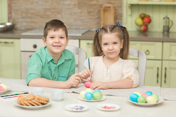 Cute brother and sister draw on the Easter eggs at the table.and laugh