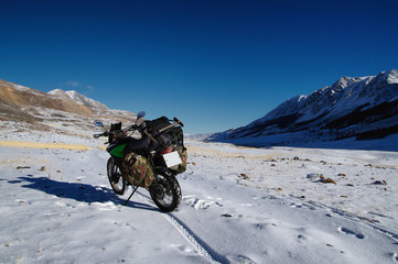 Motorcycle traveler standing on snow winter steppe in a mountain plateau in clear weather on the background of hills