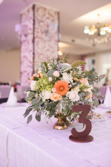 Flowers composition with orange and beige flowers and number three on the table for guests on wedding hall. Wedding table number. Rustic flower arrangement at a wedding banquet. Table set for an event