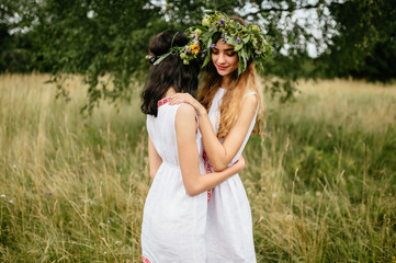 Couple of young girls in love. Beautiful Slavonic appearance cute females in traditional pagan dresses hugging each other at nature. Teenagers in rustic costumes tender feminine portrait outdoor.