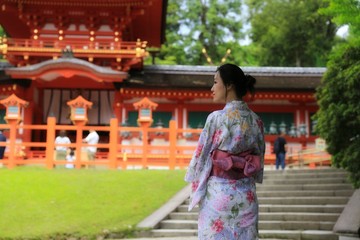 a young Japanese woman in summer kimono (yukata) standing in front of a red traditional Japanese...