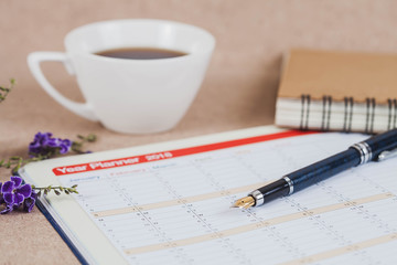 personal organizer or planner with fountain pen and hot coffee on wood table.
