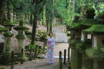 a young Japanese woman in summer kimomo (yukata) with traditional stone lanterns with lichen