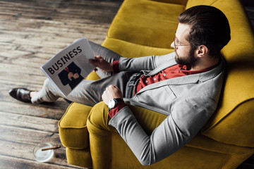 stylish man reading business newspaper and sitting on couch