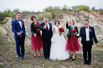 Fantastic wedding couple and bridesmaids with groomsmen drinking champagne in sand quarry.