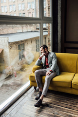 Fototapeta na wymiar stylish thoughtful man sitting on yellow sofa and looking at window