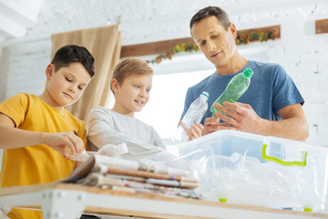 Caring about nature. Charming young man and his pre-teen sons preparing plastic bottles for...