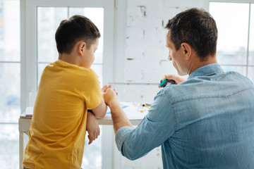 Quality time together. Caring young father showing a tape measure to his son, teaching how to use this tool while constructing something together