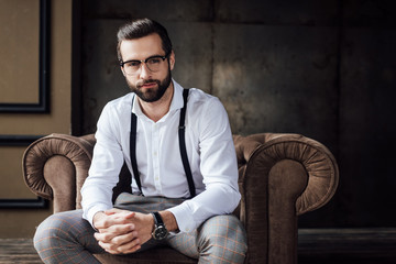 handsome stylish man in glasses and suspenders sitting in armchair