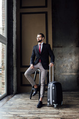 Fototapeta na wymiar elegant businessman in suit posing on stool with luggage