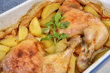 two roast chicken legs with potato and fresh green spice in a tray on a wooden table