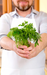 Man in the kitchen holds a bunch of fresh greens of dill and parsley. Vegetable diet is good for health.