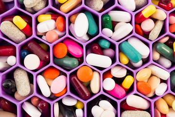 Various pills and capsules on cellular comb organizer.
