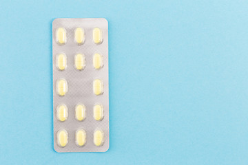 One blister of yellow pills on blue medical background with copy space.