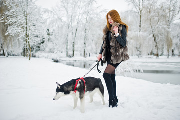 Fototapeta na wymiar Red haired girl walking at park with husky dog on winter day.