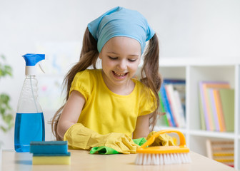 Little child girl cleaning her nursery room. Kid wiping table with yellow rag and holds spray on...