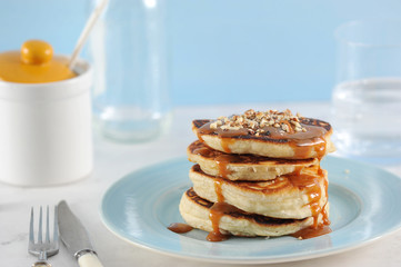 Pancakes with caramel and nuts. Pancakes are lined with a pile, poured with caramel syrup, sprinkled with nut crumbs. Near the glass with water. Close-up. Vertical orientation of the frame.