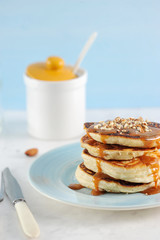 Pancakes with caramel and nuts. Pancakes are lined with a pile, poured with caramel syrup, sprinkled with nut crumbs. Next to the cutlery and sugar bowl.. Close-up. Vertical orientation of the frame.