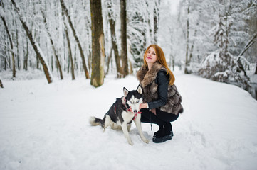 Red haired girl walking at park with husky dog on winter day.