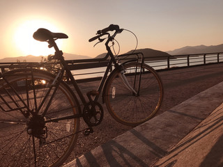 Silhouette of bicycle, fence, road and sea at sunset