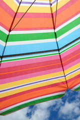 Multicolor striped beach parasols in backlit of summer sun.