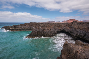 Fototapeta na wymiar Lanzarote landscape. Los Hervideros coastline, lava caves, cliffs and wavy ocean. Unidentifiable tourist are in the background