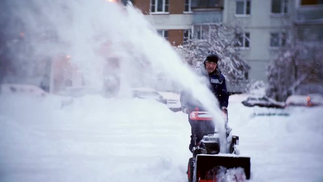 The janitor clears the track with a snowplow in the courtyard of an apartment building.