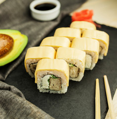 Japanese sushi rolls on a slate black board with chopsticks, soy sauce and avocado