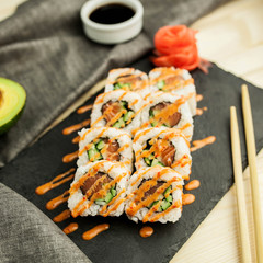 Japanese sushi rolls on a slate black board with chopsticks, soy sauce and avocado