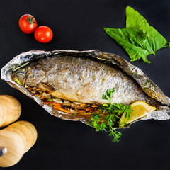 baked whole fish with vegetables and lemon in foil on a stone board - 193102091