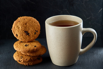 Close-up white cup of coffee with chocolate chip cookies on dark background, top view
