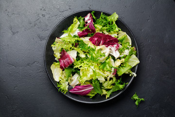 Fresh leaves of different salads in ceramic plate on black stone background. Selective focus. Top view. Copy space.