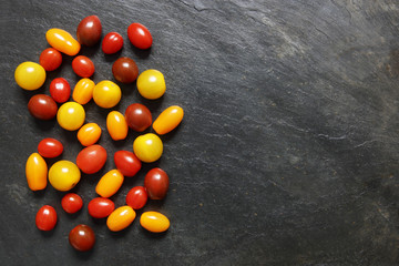 Assorted red, dark, yellow and orange small cherry tomatoes on slate © Nicholas B