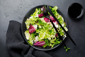 Fresh leaves of different salads in ceramic plate on black stone background. Selective focus. Top view. Copy space.