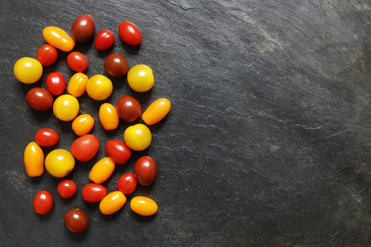 Assorted red, dark, yellow and orange small cherry tomatoes on slate