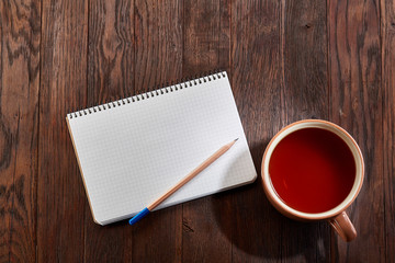 Cup of tea with cookies, workbook and a pencil on a wooden background, top view
