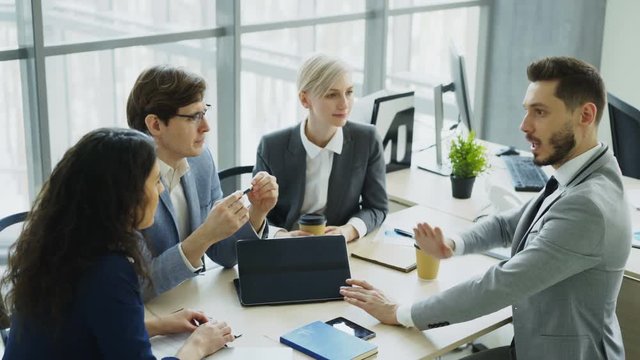 Businessman discussing future business project with male and female colleagues sitting at the table in modern office