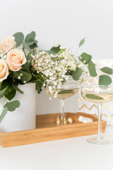 Blush wedding bouquet with roses, baby's breath and eucaluptus in wooden tray with wineglasses