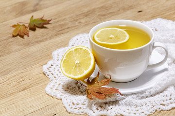 Autumn cup of tea with lemon on rustic wooden background full of bright yellow leaves, selective focus
