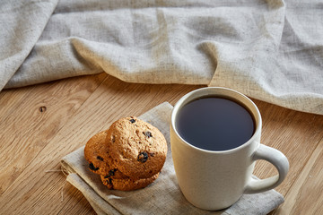 Porcelain teacup with chocolate chips cookies on cotton napkin on a rustic wooden background, top view