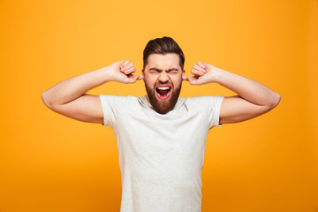 Portrait of an annoyed bearded man covering ears