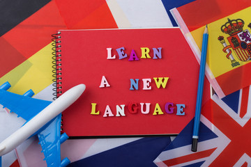 Learning languages concept - red notepad and colorful wooden letters with text "Learn a new language", flags, model airplane