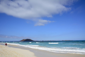Eine Person an einem hellen Sandstrand am Meer vor einer Insel.
