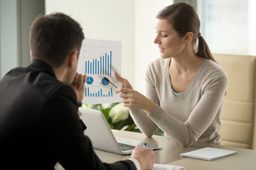 Attractive millennial businesswoman presenting company financial indicators, telling business partner about investment plan, showing document with project positive stats sitting at office desk